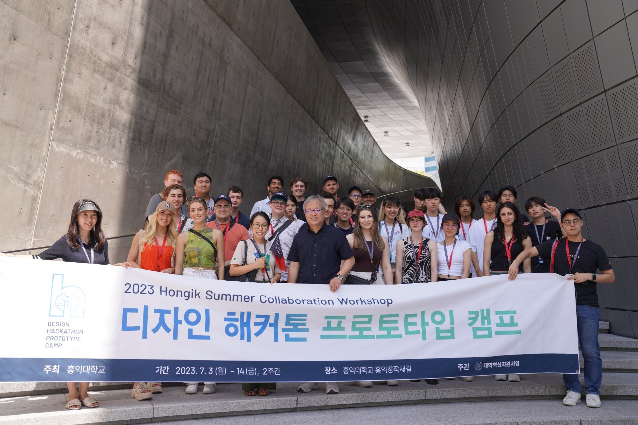 A large group of students and staff stand outside holding a large Hongik University banner 