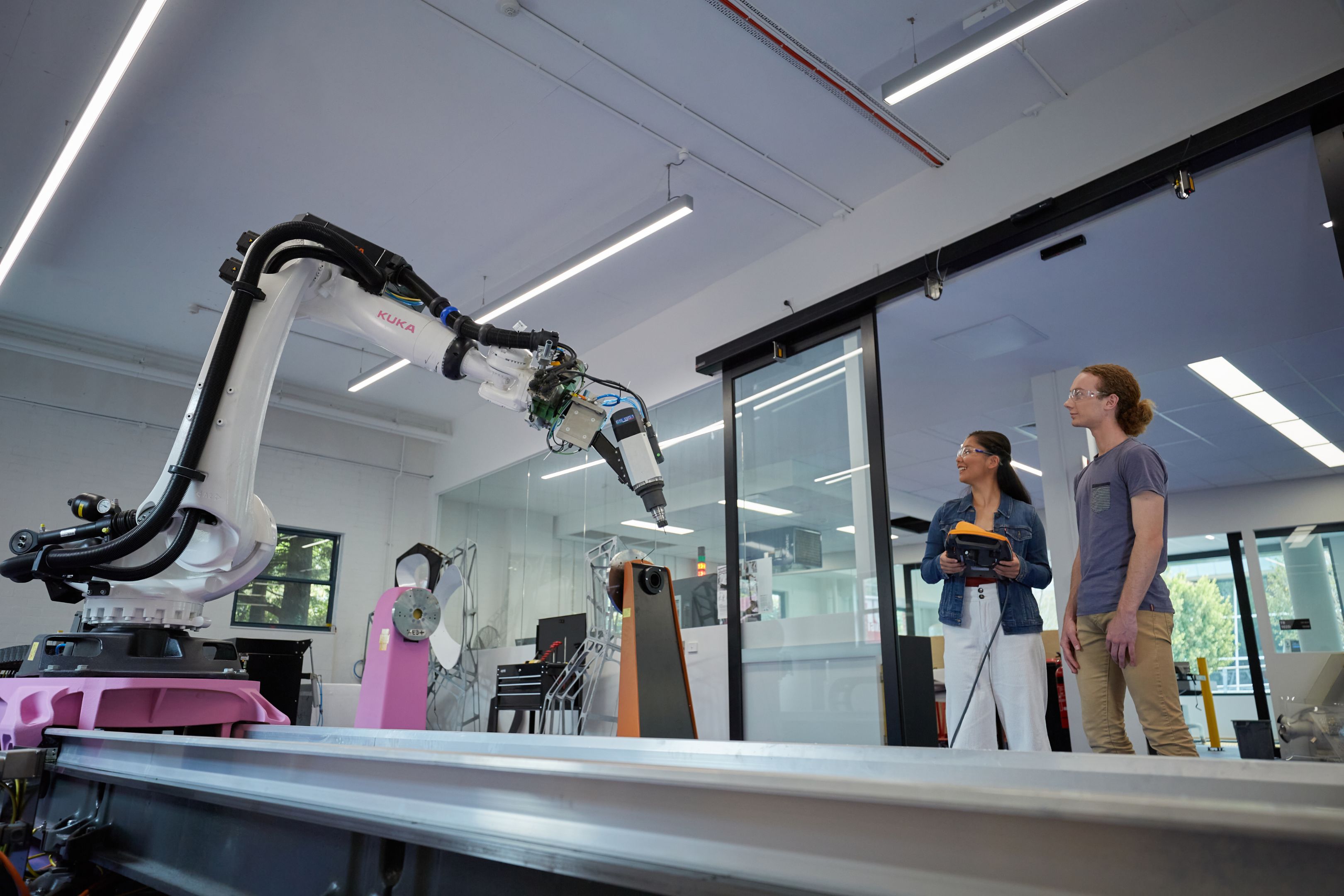 Male and female student in Protolab standing next to Kuka robotic arm
