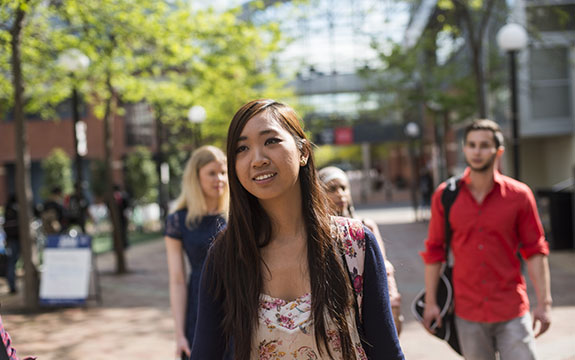 A female student on campus with blurred students in the background. 