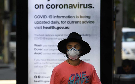 Person wearing a face mask in front of a coronavirus information sign