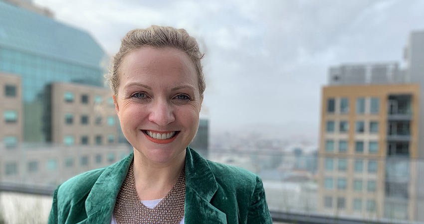 Amy dressed in a green blazer corporate buildings behind her.	
