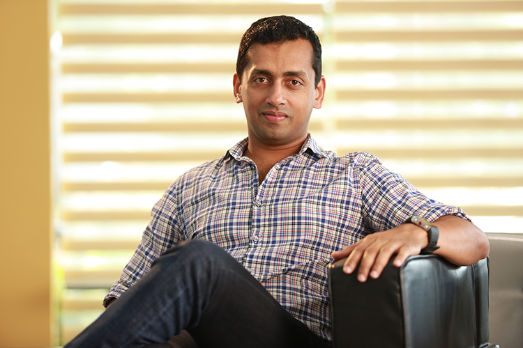Arun in a checkered shirt sitting in a chair against a sun-yellow background.