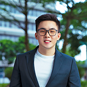 Ian standing tall in business attire against a background of trees and blue sky. 
