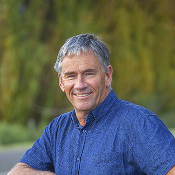John standing outside in a blue shirt smiling. 