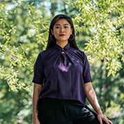 Namira standing outside in a dark purple top with green trees in the background.