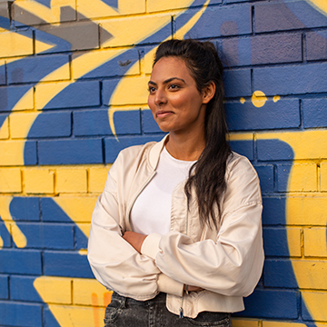 Salonie standing against a brick wall with yellow and blue graffiti.  