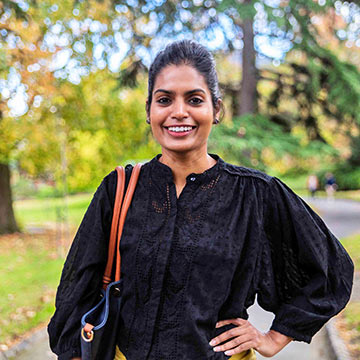 Sumundu stands smiling in a park in a dark top.