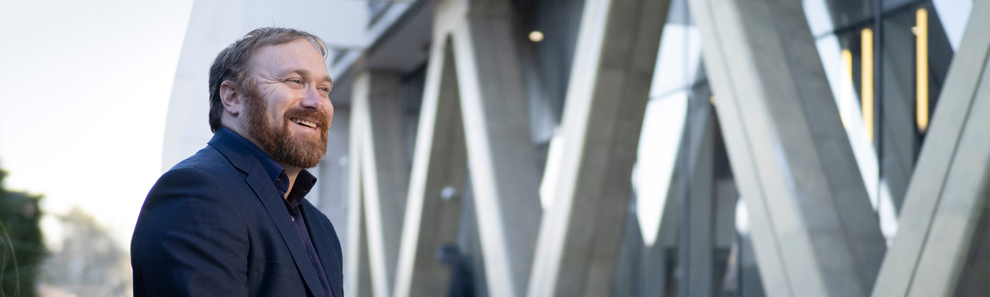 A proud and smiling businessman, standing in front of a modern building.