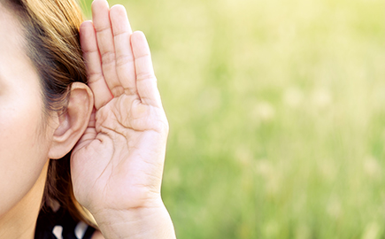 A lady with her hand up to her ear to signify hearing
