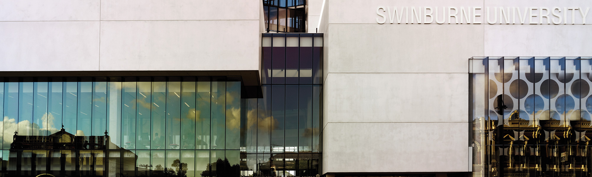 A grey building facade featuring Swinburne University signage and sunlight reflecting off the windows.